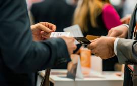 Scène de networking animée où deux professionnels échangent des cartes de visite, entourés d'autres participants dans un cadre d'événement d'affaires |  COPYTOP