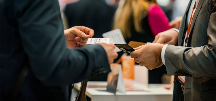 Scène de networking animée où deux professionnels échangent des cartes de visite, entourés d'autres participants dans un cadre d'événement d'affaires |  COPYTOP